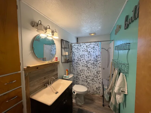 Modern bathroom featuring a floating vanity with rectangular vessel sink and matte black faucet, large circular mirror with integrated lighting, terrazzo-pattern tile shower surround, wood-finish flooring, and soft-close cabinetry with ample storage