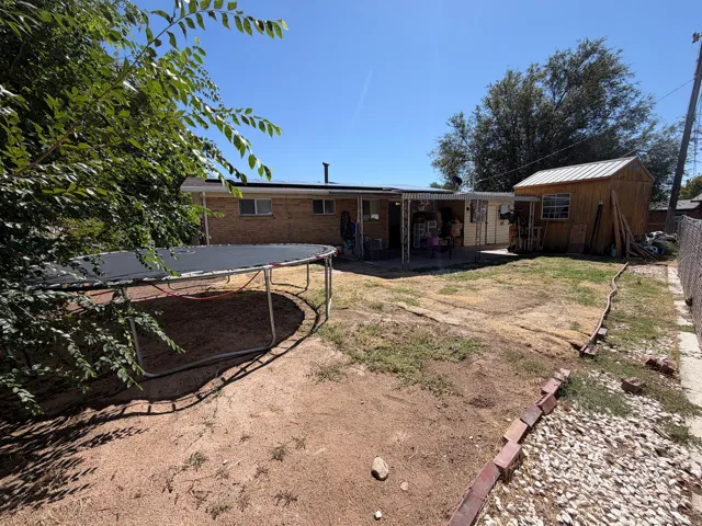 Rear brick exterior with a covered patio, a wood-sided shed with a metal roof, and chain-link fencing