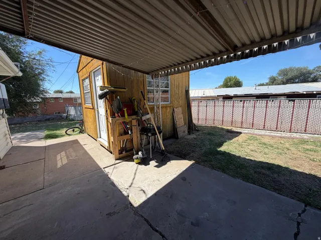 Covered patio with corrugated metal roof, concrete slab flooring, and adjacent wood-sided shed