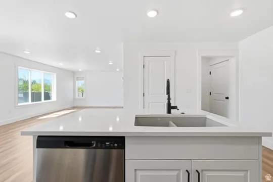 White kitchen island with a built-in stainless steel dishwasher, undermount sink, and matte black faucet