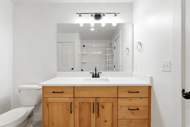 Natural wood vanity with multiple drawers, white countertop, rectangular undermount sink, and matte black faucet