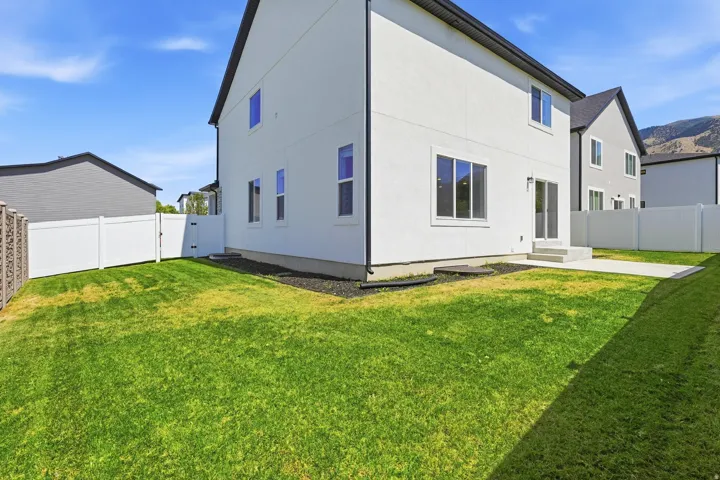 Expansive backyard featuring a lush lawn, white vinyl fencing, and a concrete patio