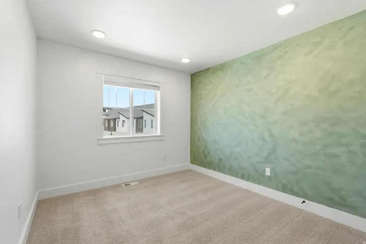 Recessed ceiling lighting, textured accent wall, light-toned carpeting, white window trim, and white baseboards