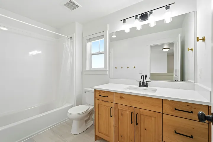 Bathroom featuring a wood-finish vanity with a white countertop, matte black faucet, and a large mirror