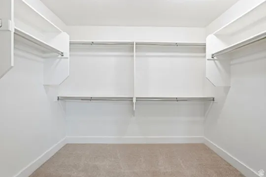 Built-in shelving with multiple hanging rods, white walls, and carpet flooring