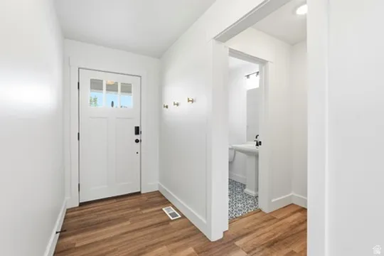 Entryway featuring wood-finish flooring, a contemporary front door with clear glass panes, and a bright white paint scheme