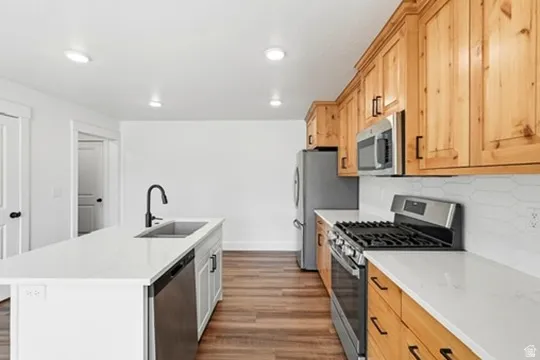Kitchen featuring wood-finish flooring, recessed lighting, a kitchen island with an undermount sink, white countertops, and wood cabinetry with matte black hardware