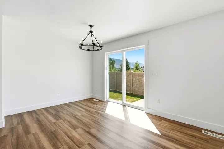 Wood-finish flooring, white walls, black chandelier, sliding glass door, and a private rear yard with a stone fence
