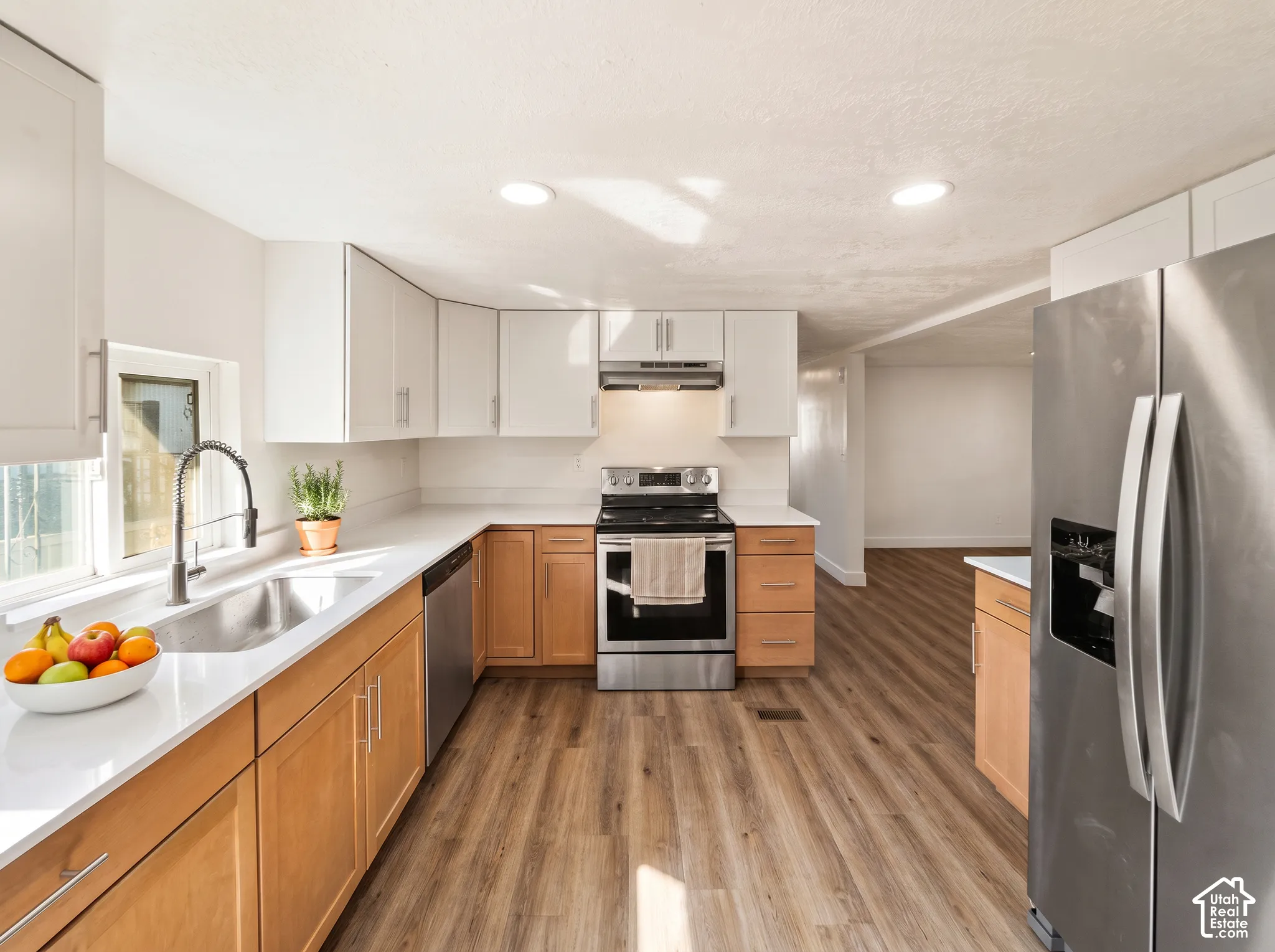 Updated kitchen featuring stainless steel appliances, light-toned upper cabinetry, natural wood-finish lower cabinetry, and wood-finish flooring