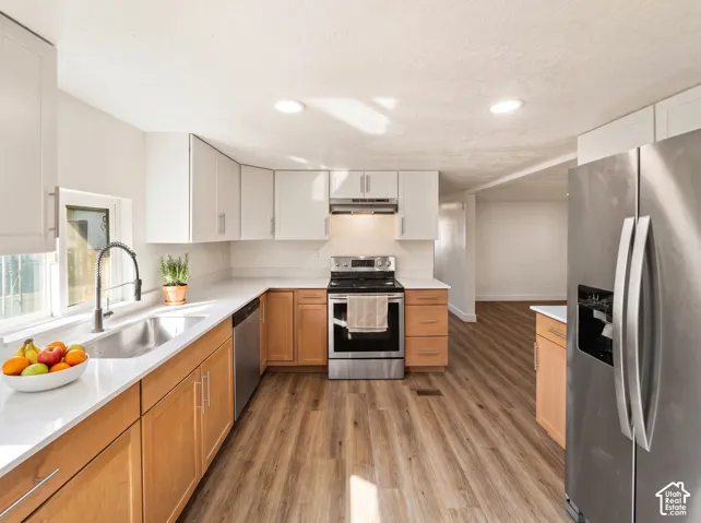 Updated kitchen featuring stainless steel appliances, light-toned upper cabinetry, natural wood-finish lower cabinetry, and wood-finish flooring