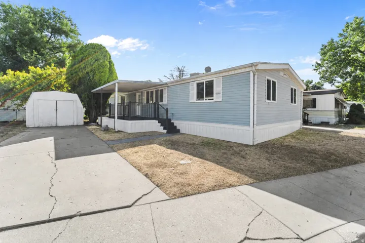 Light blue siding exterior with white trim, covered front porch, concrete driveway, and detached storage shed