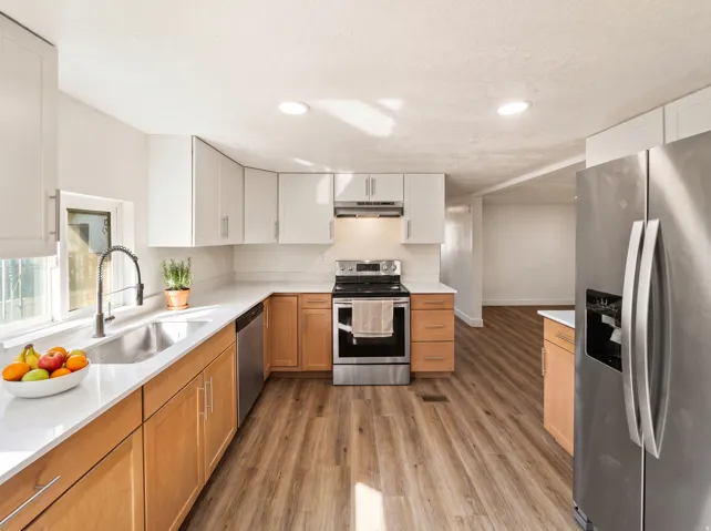 Updated kitchen featuring stainless steel appliances, light-toned upper cabinetry, natural wood-finish lower cabinetry, and wood-finish flooring