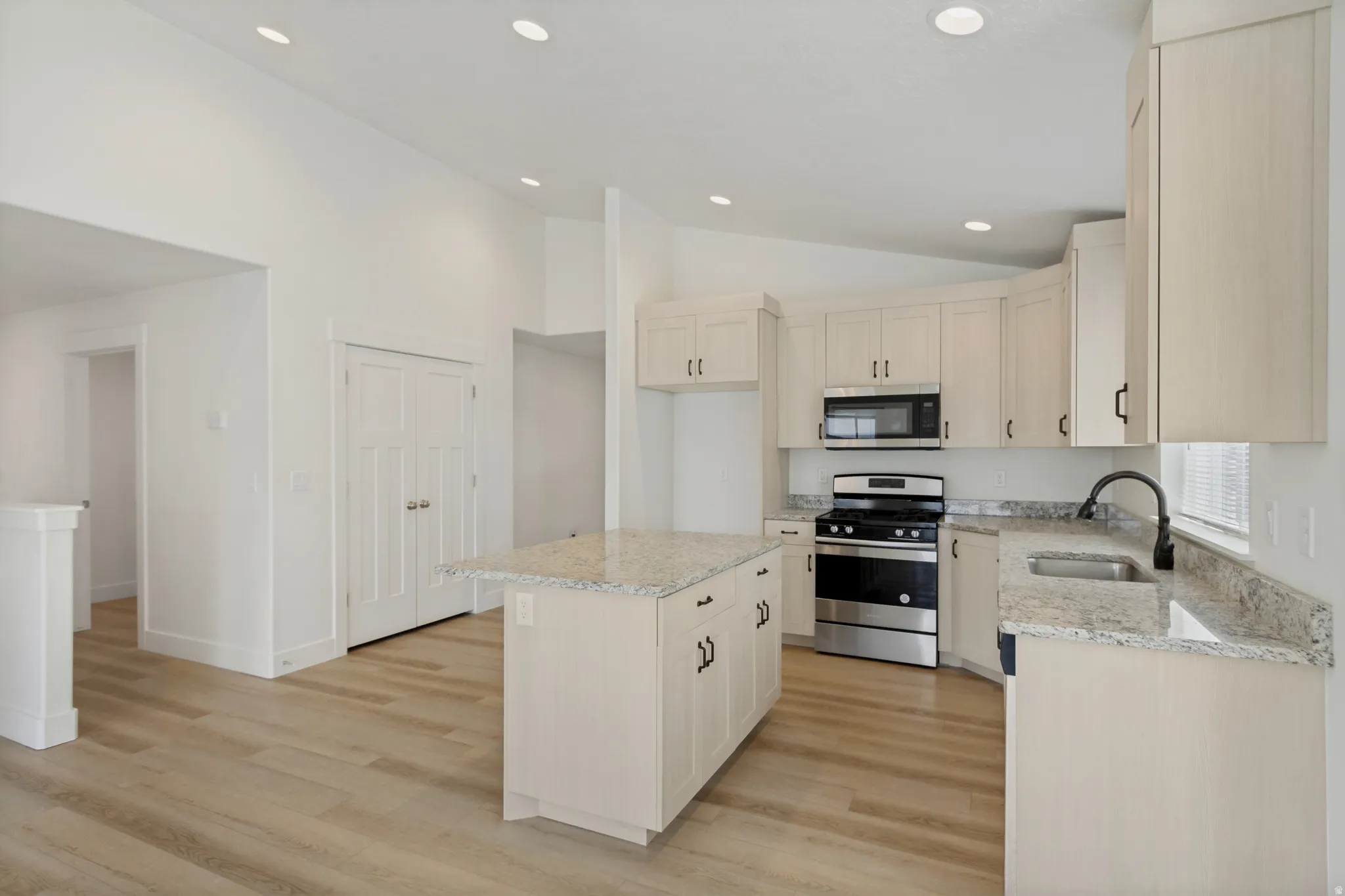 Kitchen featuring light wood-finish flooring, recessed lighting, light-toned cabinetry, stainless steel appliances, and granite countertops