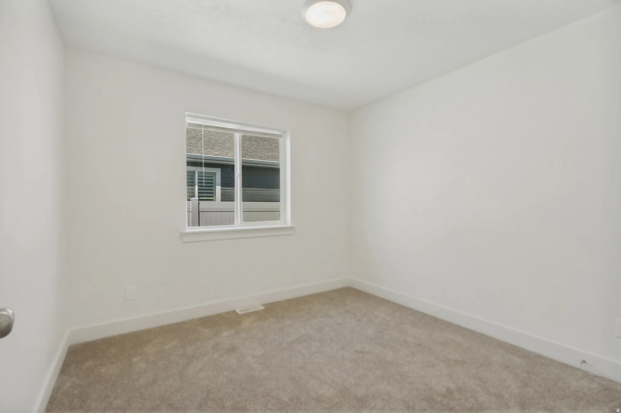 Neutral color palette, window with white blinds, flush mount ceiling light, light-toned carpet, and white trim