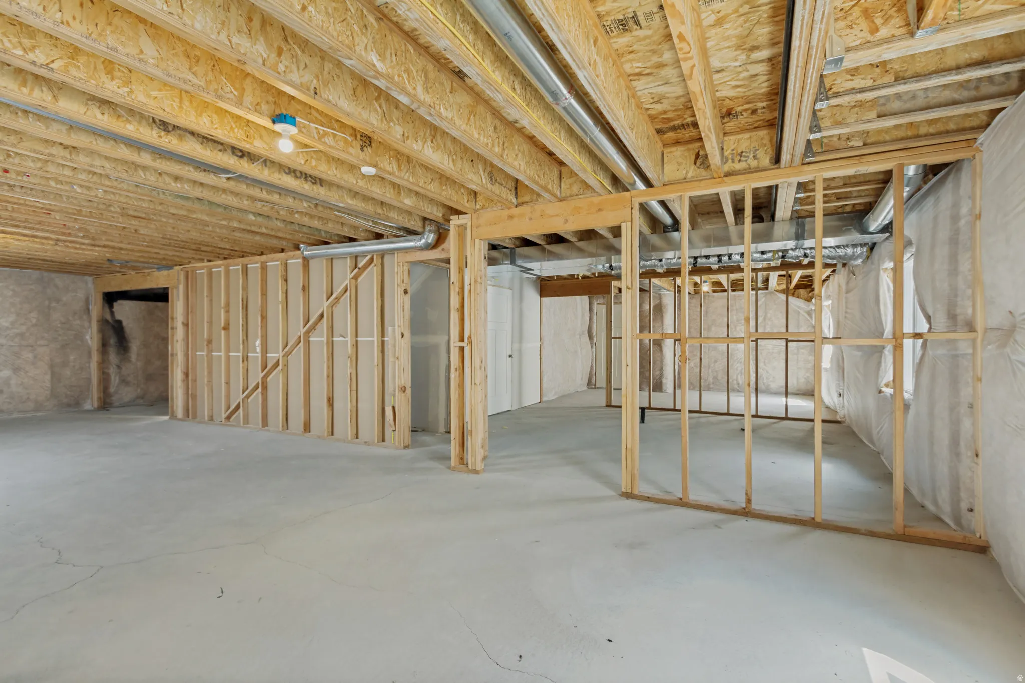 Unfinished basement with concrete flooring, exposed wood ceiling joists, and framed partition walls