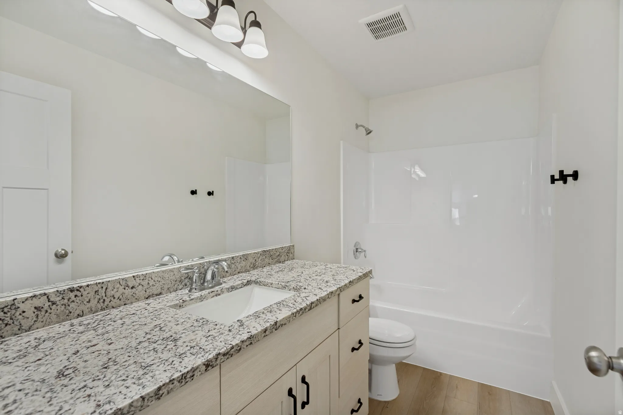 Granite-style countertop with integrated sink, chrome faucet, white flat-panel cabinetry, and wood-finish flooring