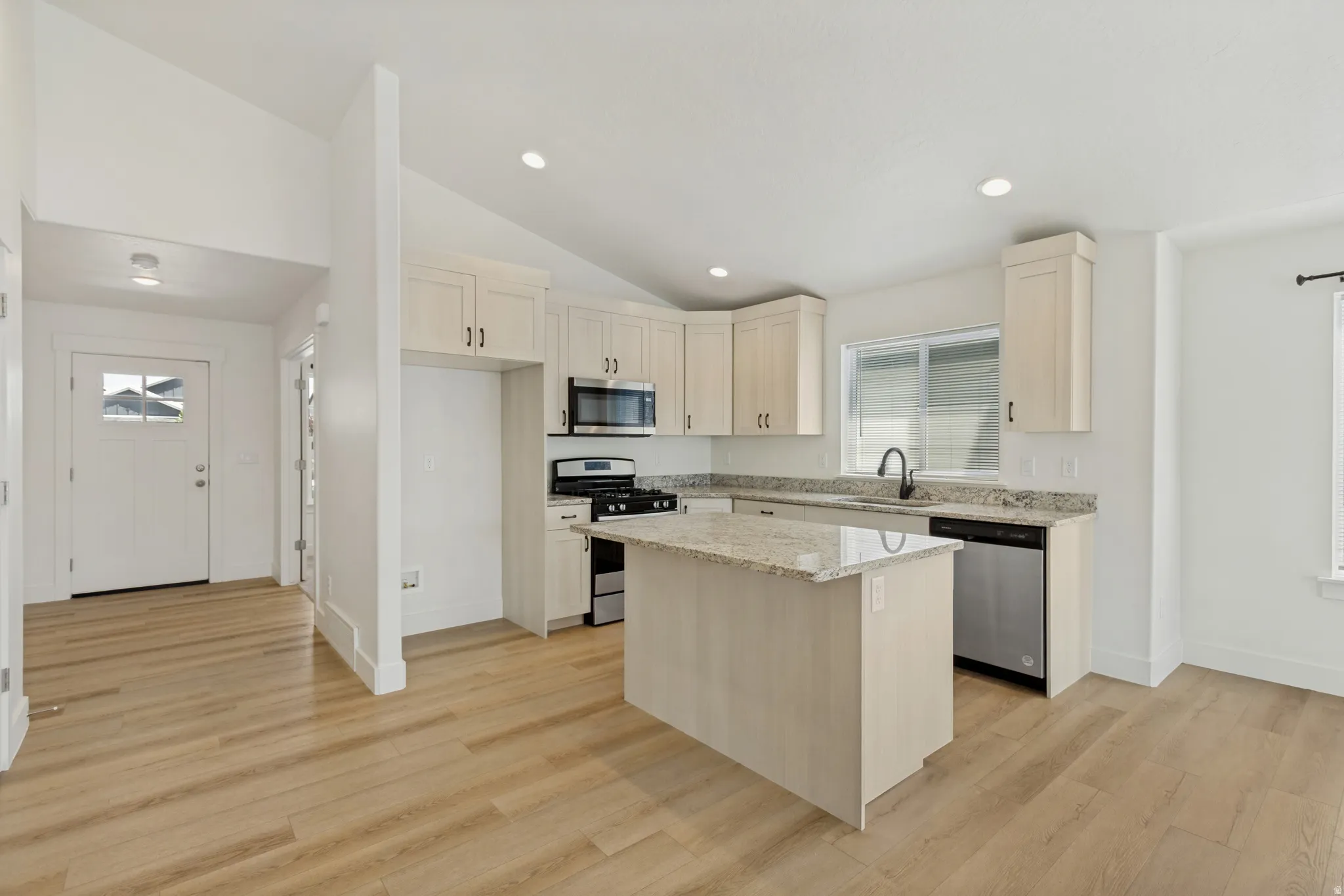 Kitchen featuring light wood-finish cabinetry, a central island, stainless steel appliances, and granite countertops
