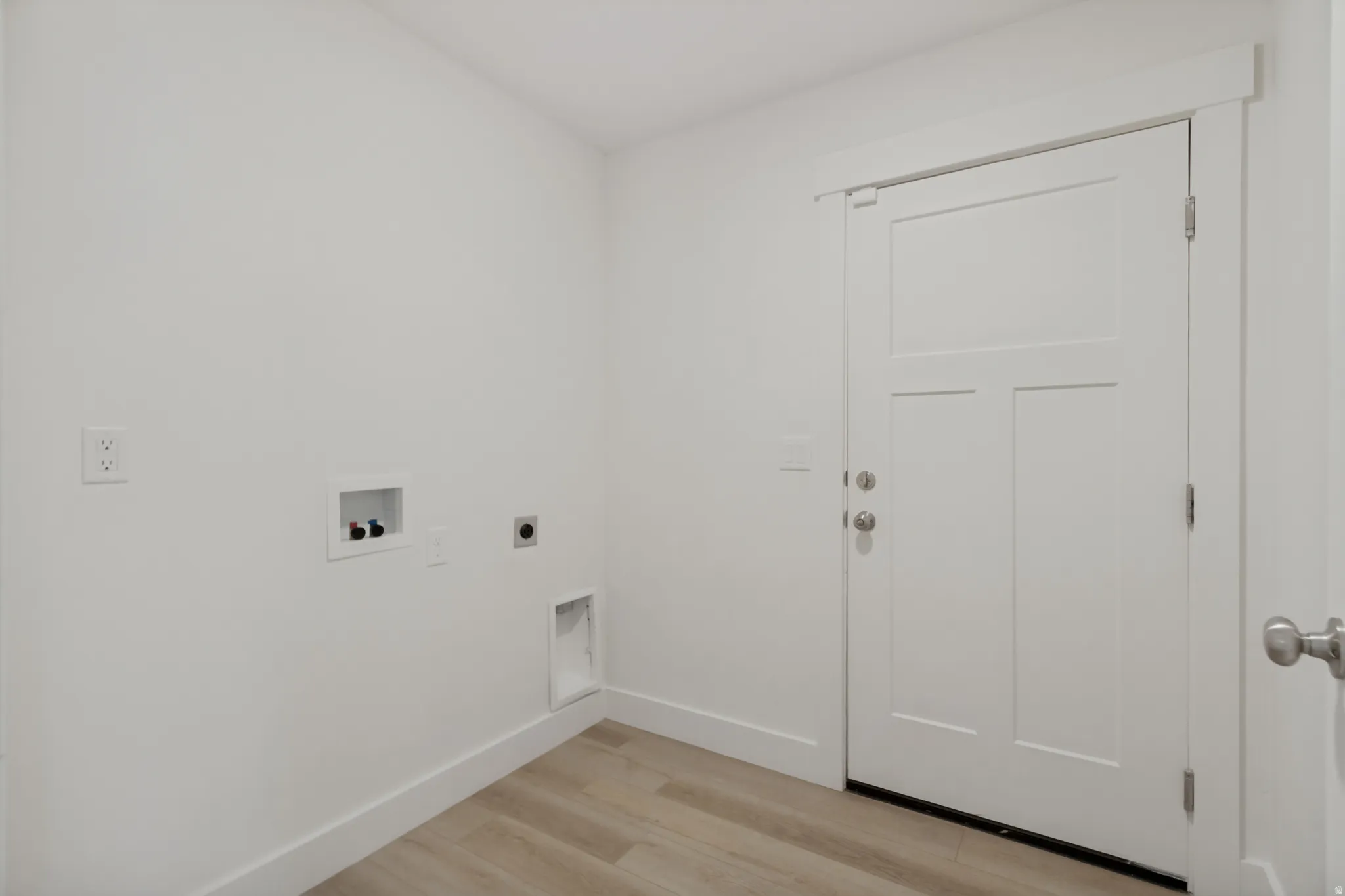 Light wood-finish flooring, white walls, and a three-panel door with brushed nickel hardware