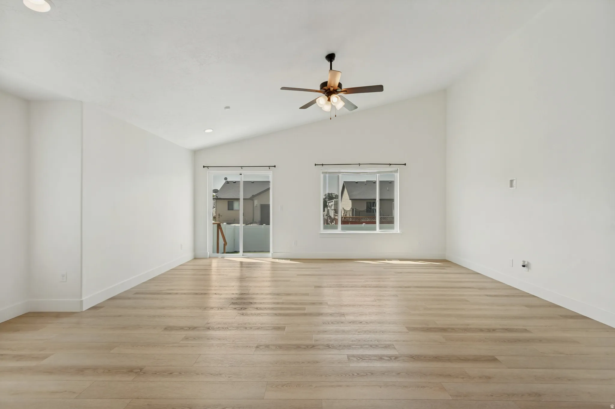 Vaulted ceiling, wood-finish flooring, recessed lighting, ceiling fan, sliding glass door, and large window