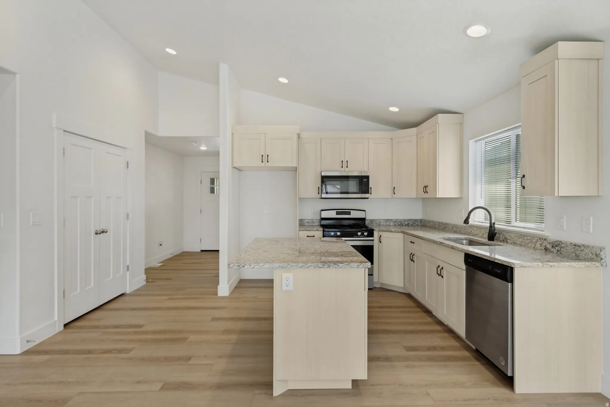 Kitchen featuring light cabinetry, stainless steel appliances, speckled countertops, and wood-finish flooring