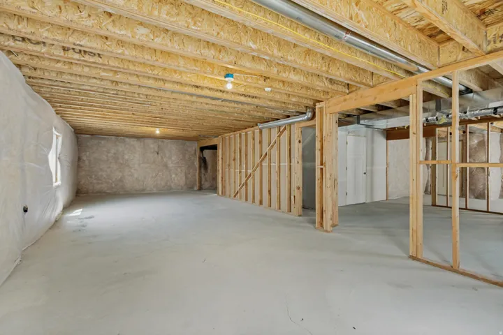Unfinished basement featuring exposed wood joists, concrete flooring, and framed interior walls