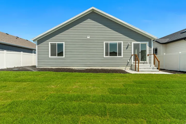 Spacious backyard with a vibrant green lawn, gray siding exterior, white vinyl fencing, and a concrete patio with steps