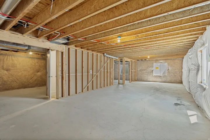 Unfinished lower level with exposed ceiling joists, concrete flooring, and roughed-in framing for future rooms