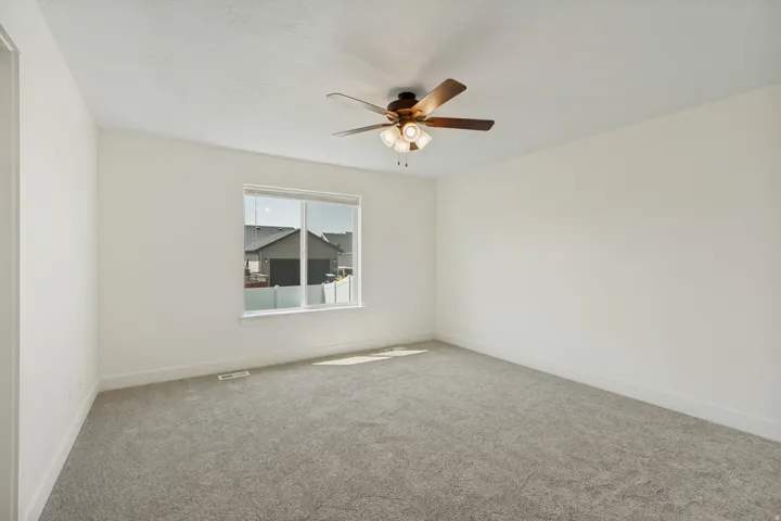 Light gray carpet flooring, white painted walls, a white framed window, and a ceiling fan with integrated lighting