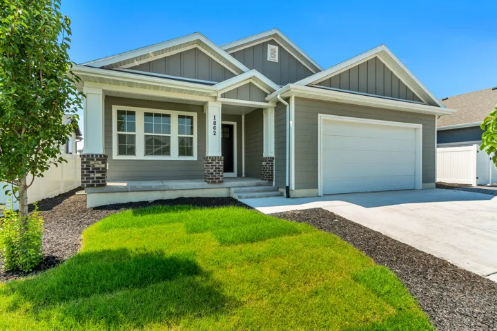 Contemporary single-story residence with gray siding, white trim, a covered front porch with brick-accented columns, a two-car garage, and a manicured lawn