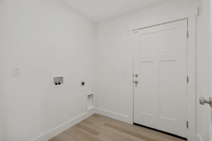 Light wood-finish flooring, white walls, and a three-panel door with brushed nickel hardware