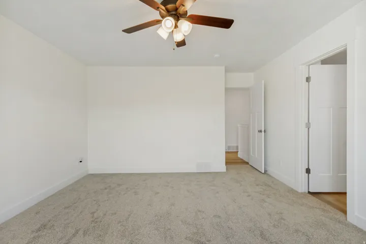 Neutral tone wall paint, textured carpeting, ceiling fan with integrated lighting, white trim, and white paneled doors