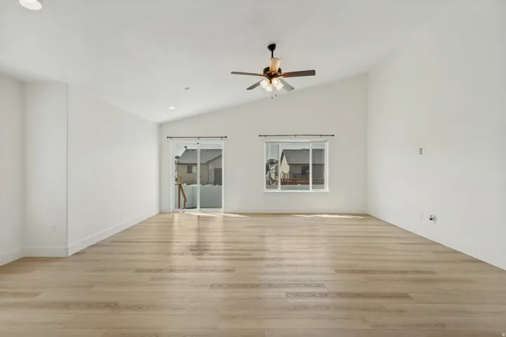 Vaulted ceiling, wood-finish flooring, recessed lighting, ceiling fan, sliding glass door, and large window