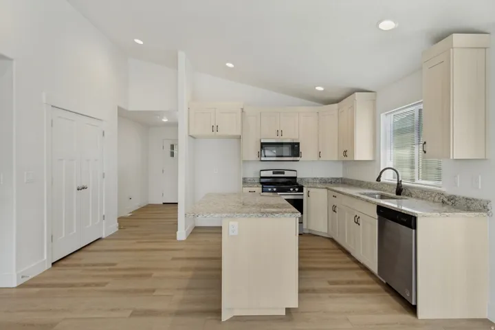 Kitchen featuring light cabinetry, stainless steel appliances, speckled countertops, and wood-finish flooring
