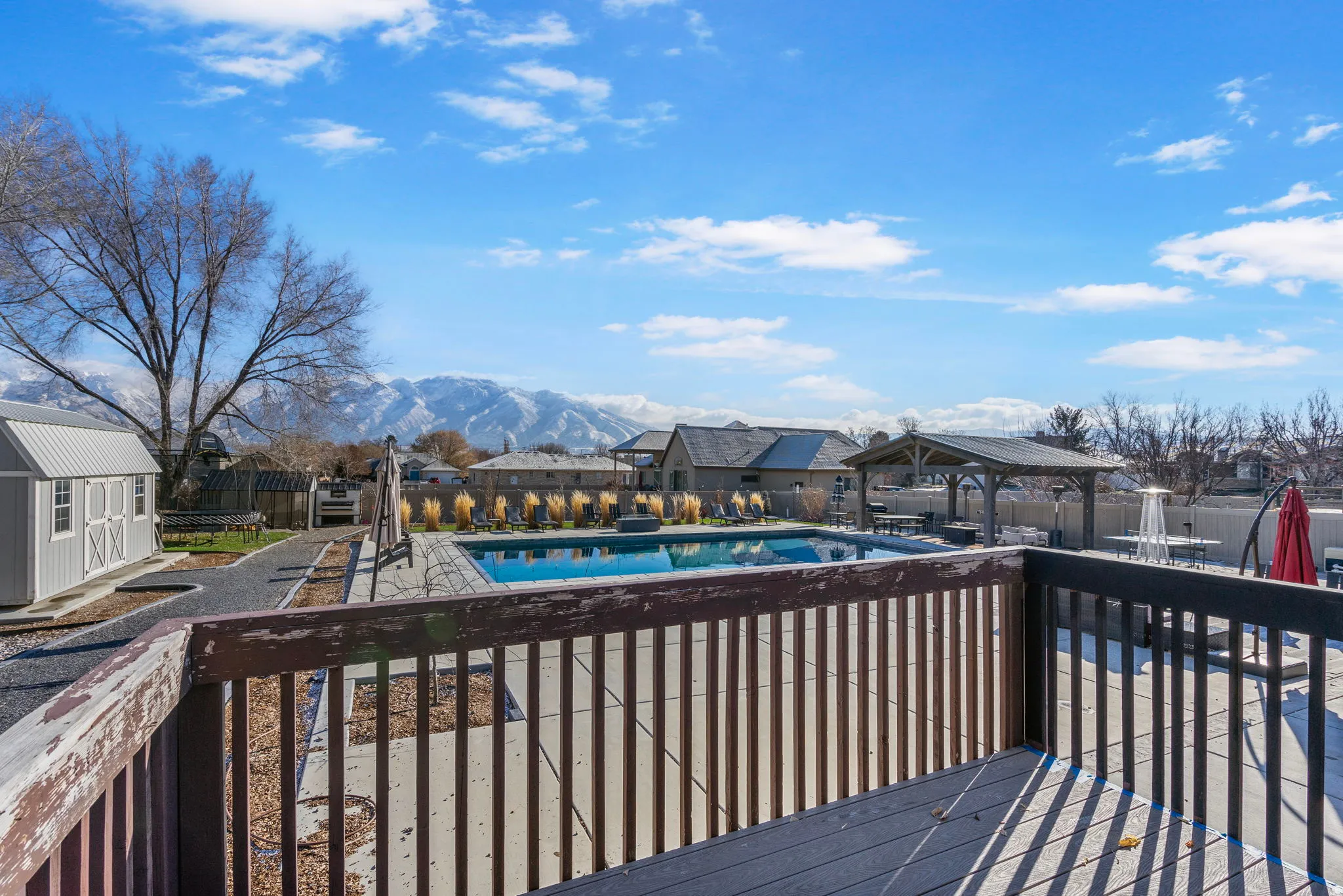 Expansive outdoor deck with a private swimming pool, concrete pool surround, built-in gazebo, and mountain backdrop
