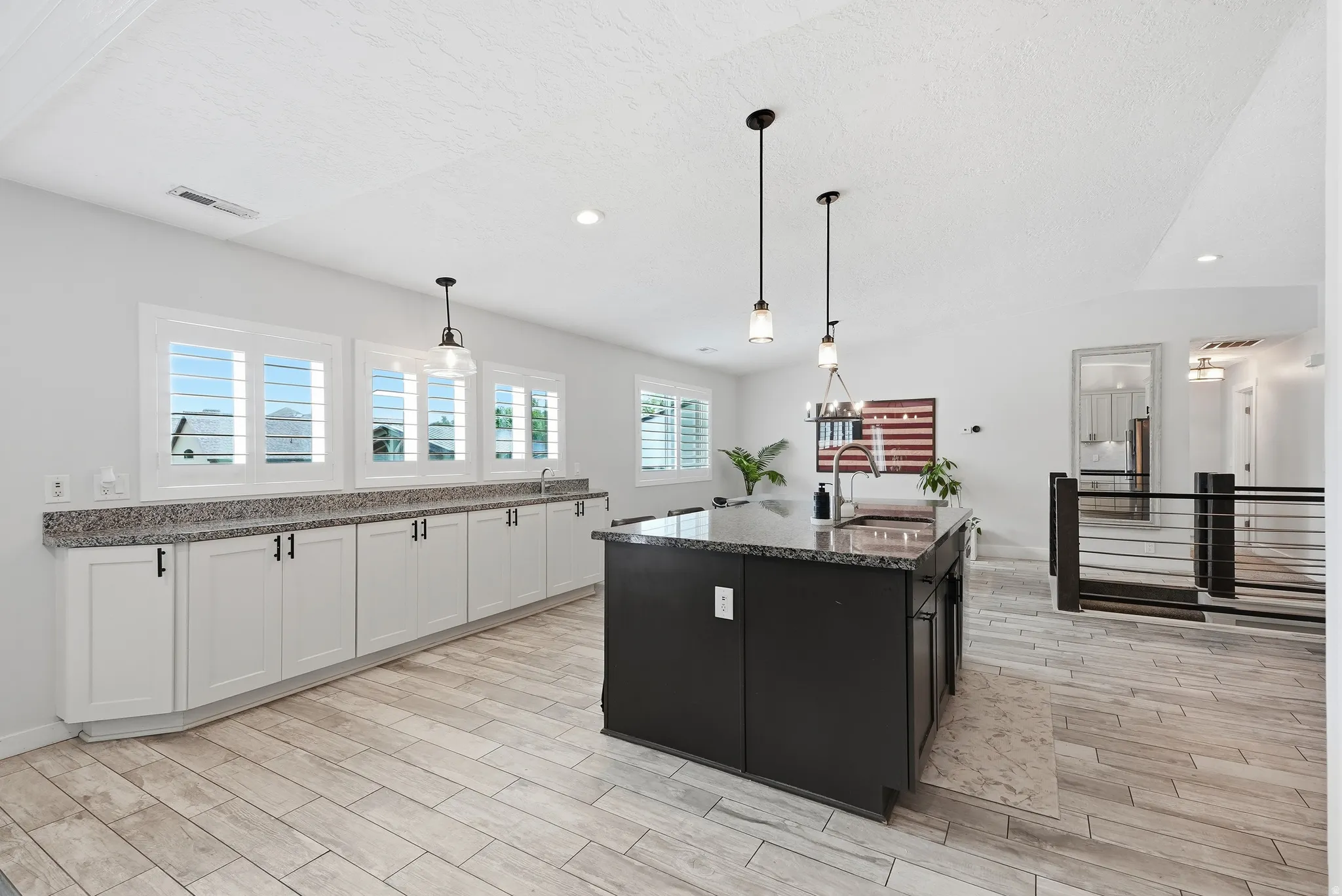 Modern kitchen featuring white shaker cabinetry, granite countertops, a dark-toned island, and pendant lighting