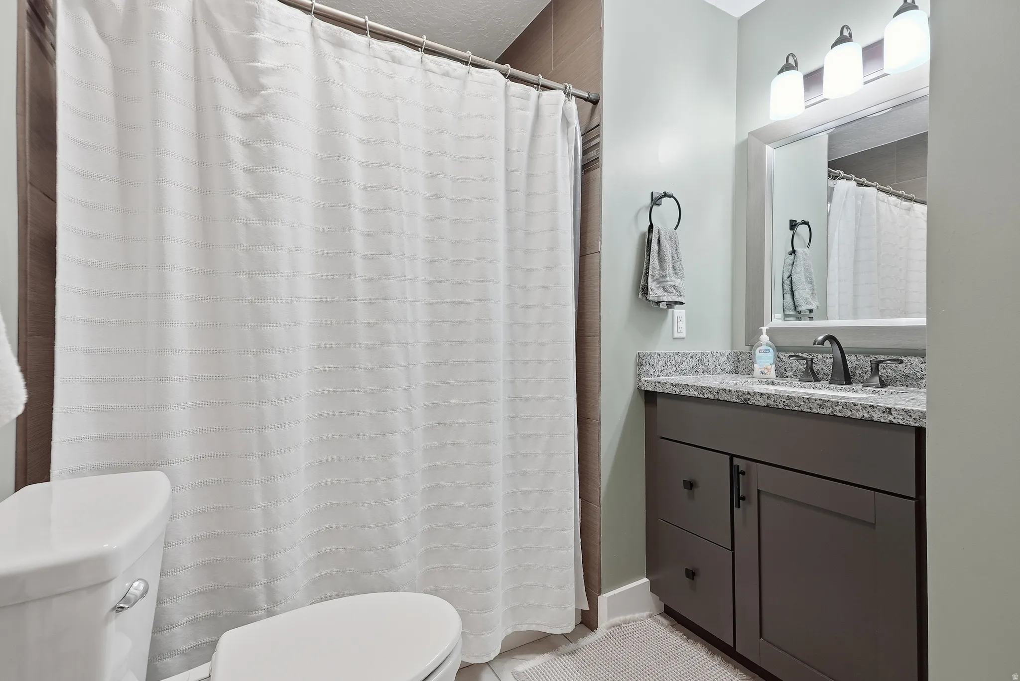 Contemporary bathroom featuring a dark wood-finish vanity with dual-sink configuration, granite countertop, and polished chrome fixtures