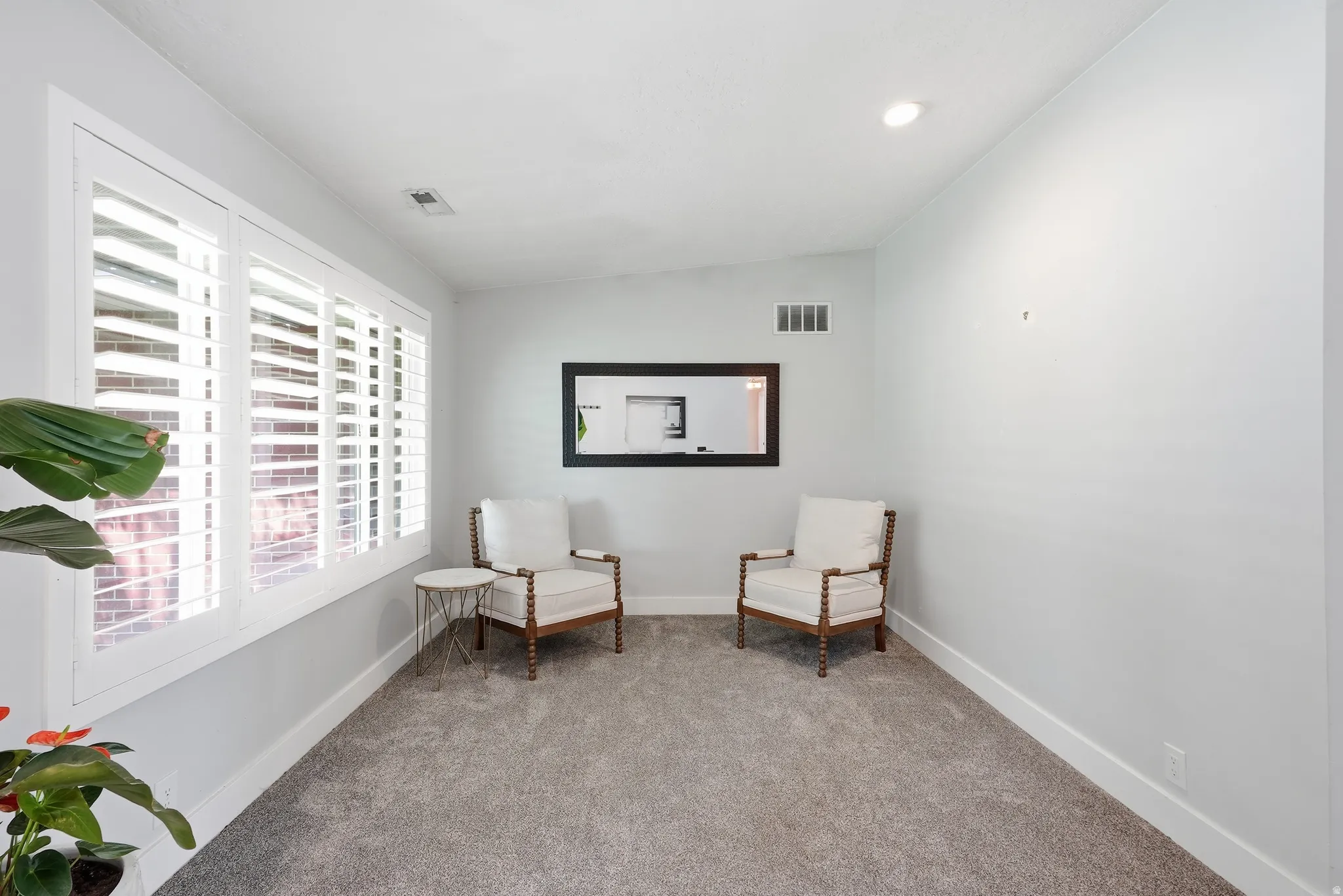Recessed lighting illuminates a space featuring gray carpet flooring and white window shutters