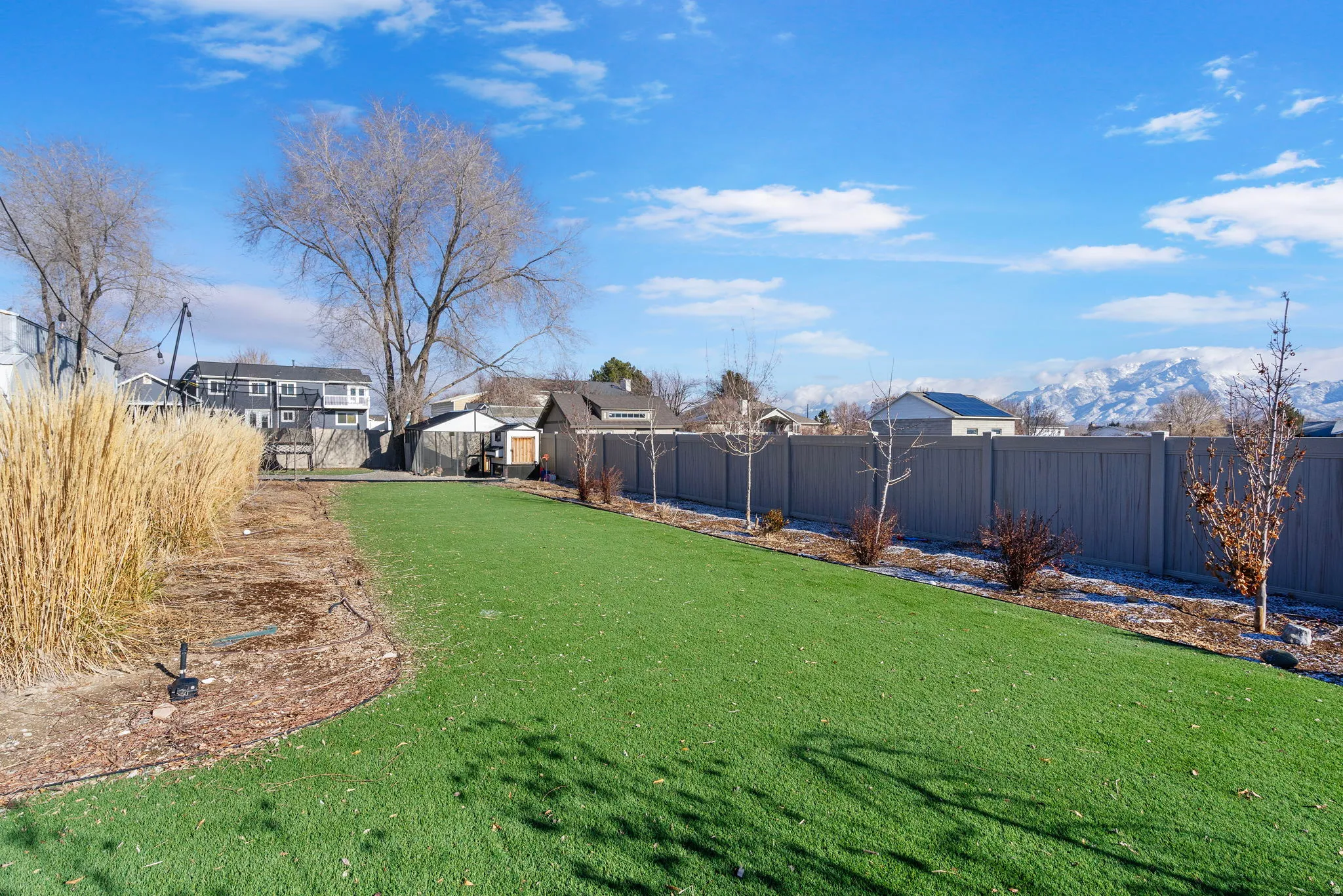 Expansive lawn with artificial turf, mature trees, a privacy fence, and mountain scenery