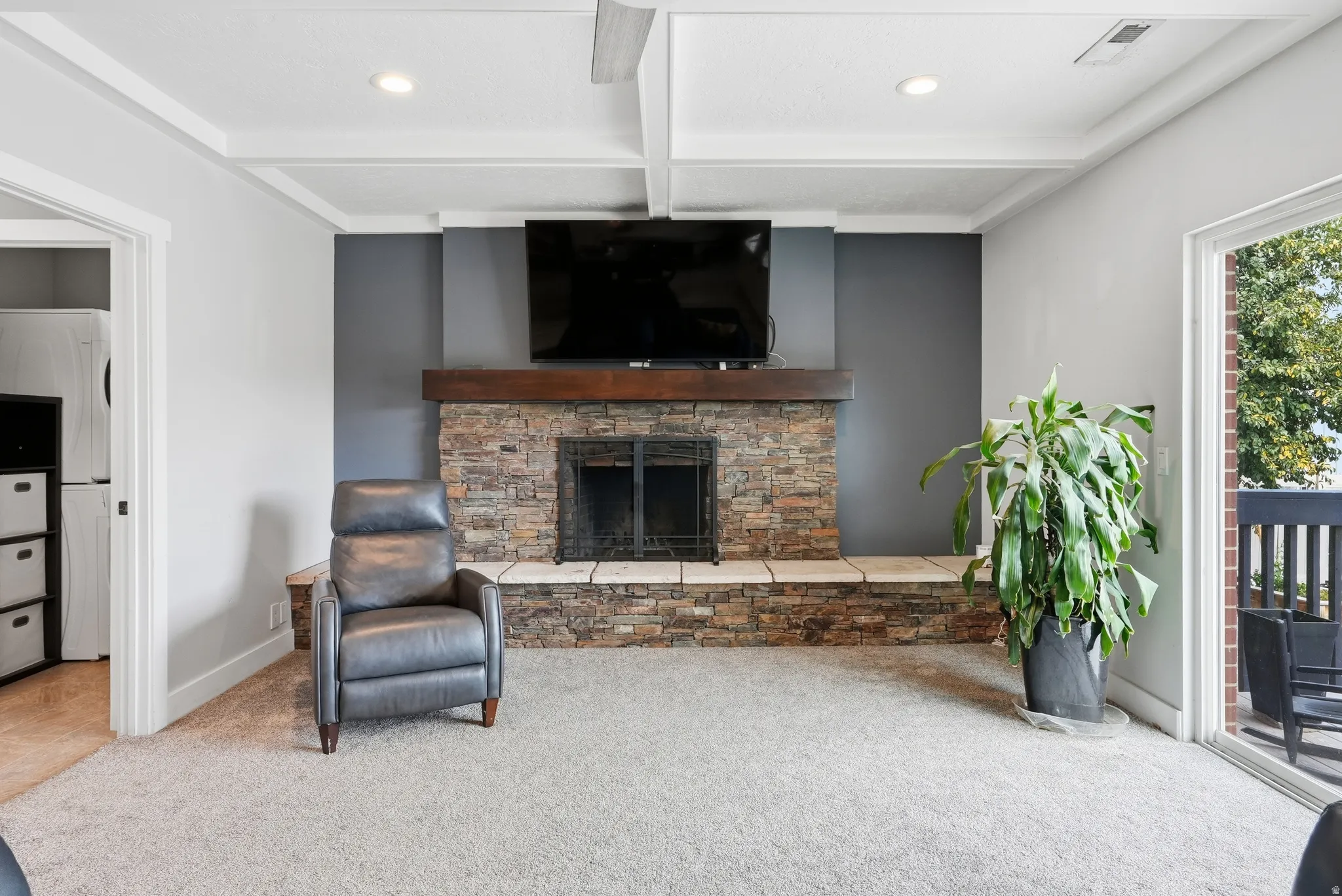 Stone-clad fireplace with a wood mantle, coffered ceiling, recessed lighting, and sliding glass door