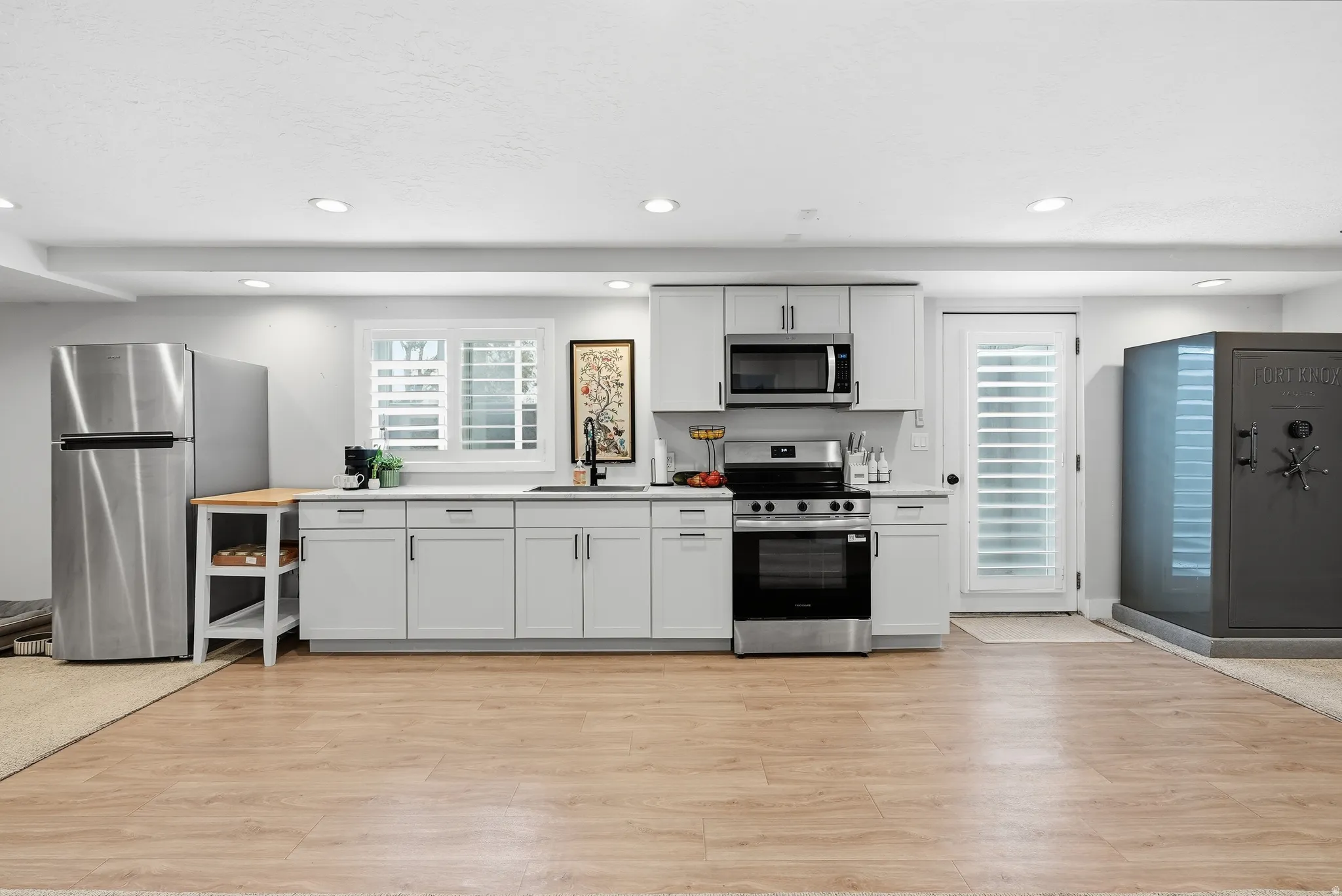 Modern kitchen featuring stainless steel appliances, white cabinetry with ample storage, black gas range with built-in microwave, wood-finish flooring throughout, and recessed ceiling lighting