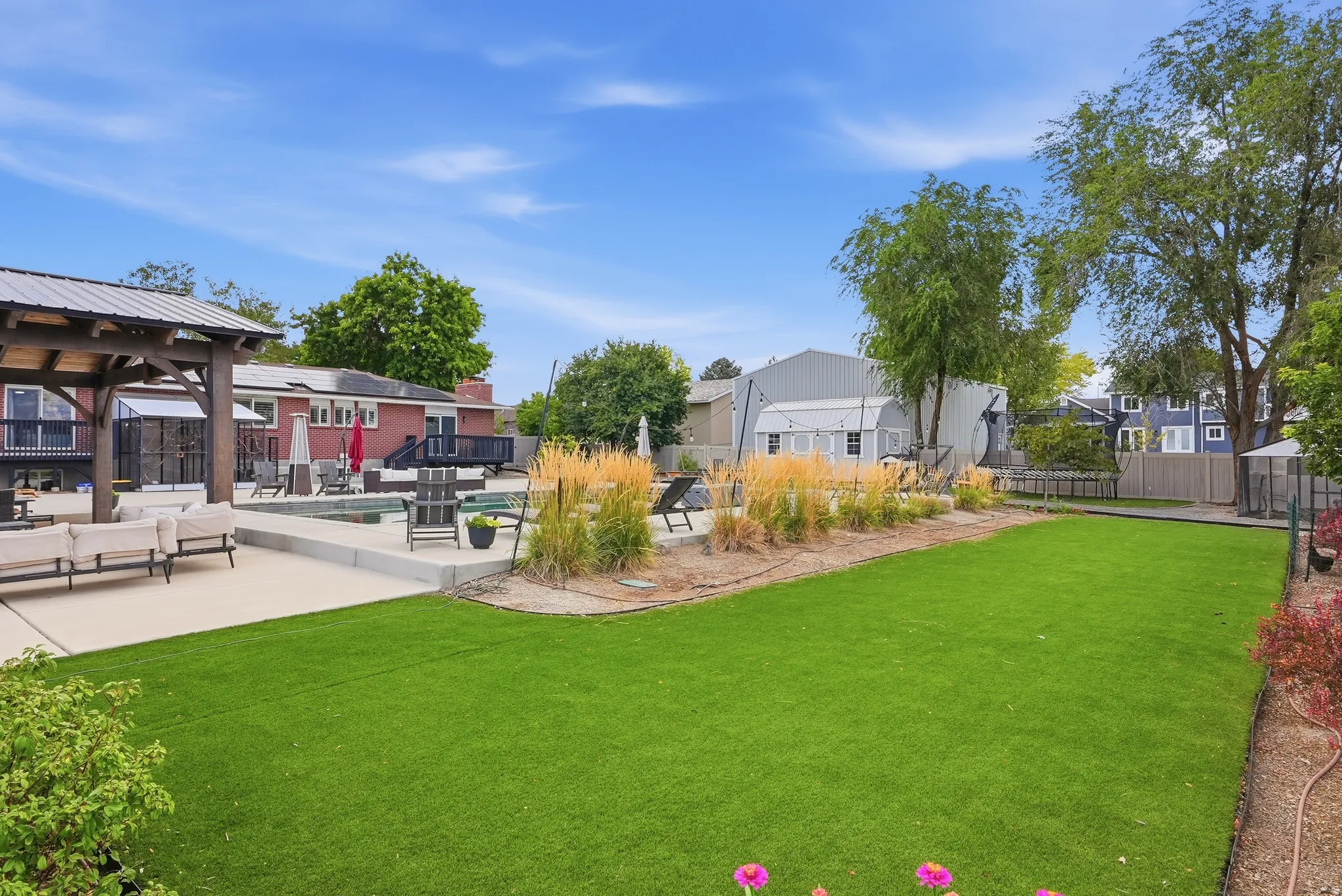Expansive outdoor space featuring a rectangular swimming pool, concrete patio, a covered pergola, and an artificial turf lawn