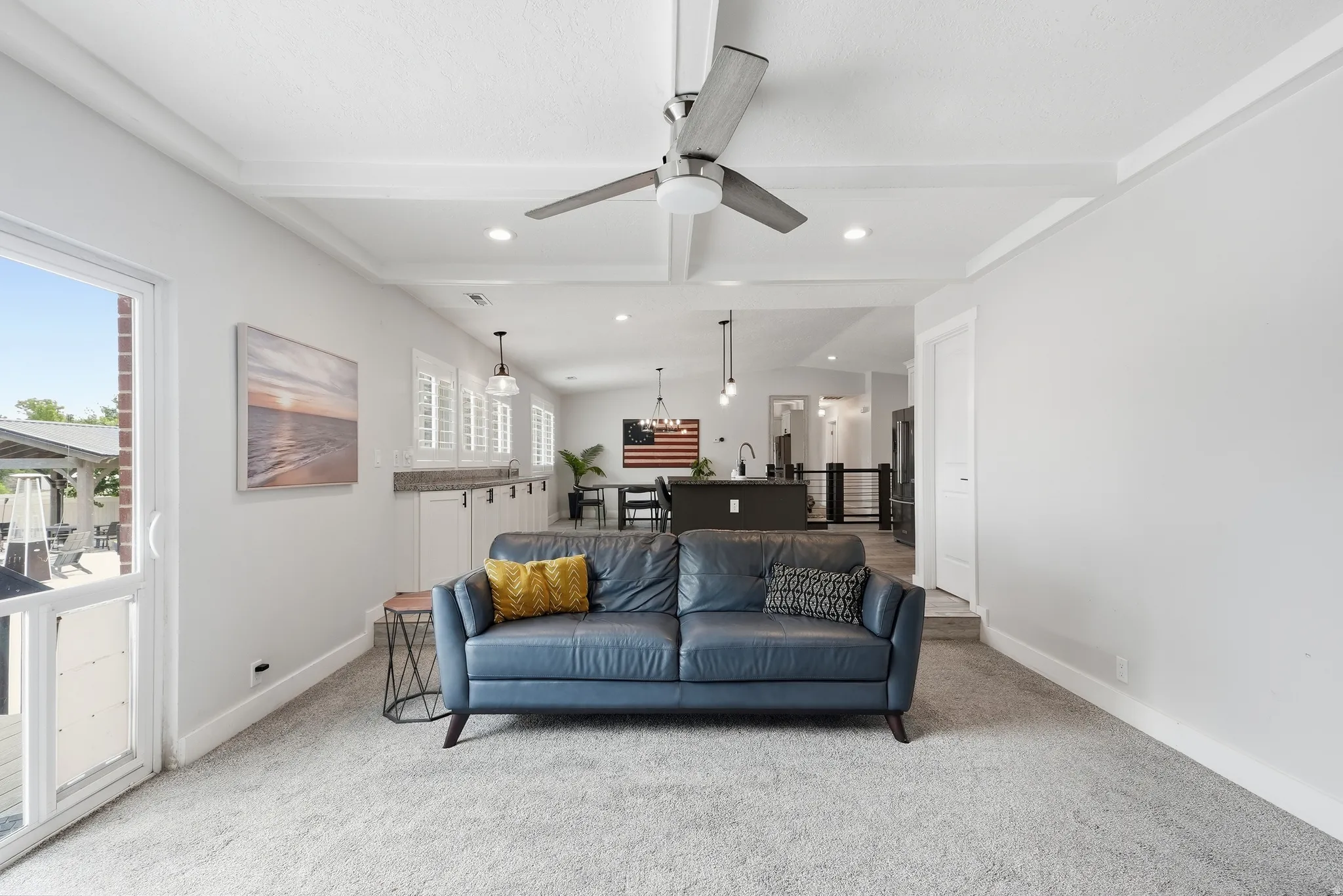 Open-concept living area featuring a blue upholstered sofa, light neutral carpeting, recessed ceiling lighting, and a ceiling fan