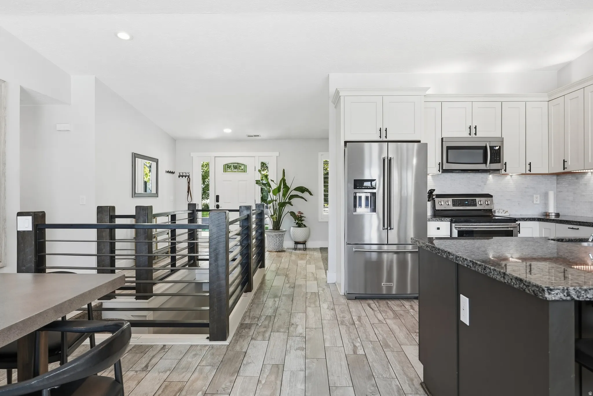 Kitchen featuring white shaker cabinetry, stainless steel appliances, dark granite countertops, and wood-finish flooring