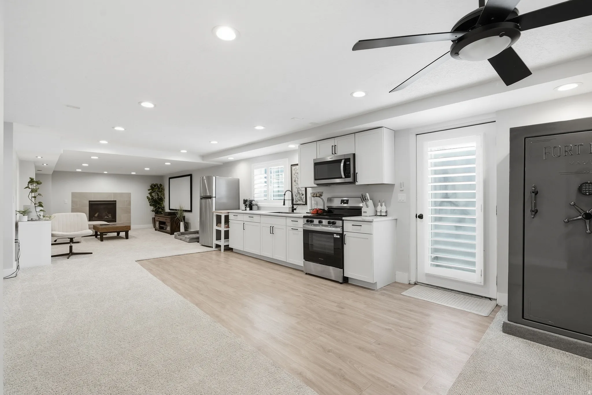 Open-concept living space with recessed lighting, a fireplace, and a kitchen featuring white cabinetry and stainless steel appliances