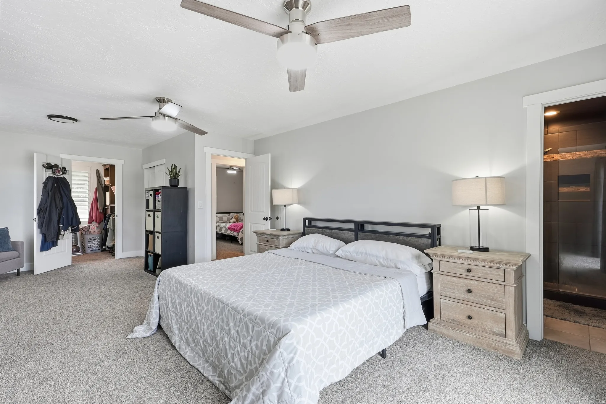Carpeted flooring, two ceiling fans, built-in shelving, white paneled doors, and a shower enclosure with dark-toned tile