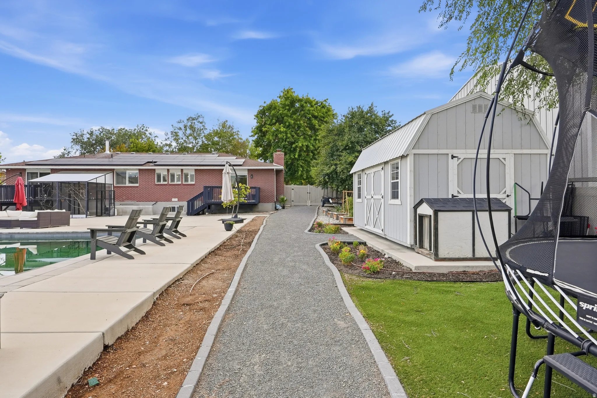 Thoughtfully designed outdoor living space featuring a wide paved pathway, manicured lawn with mature landscaping, and modern structures including a brick residence and contemporary outbuildings