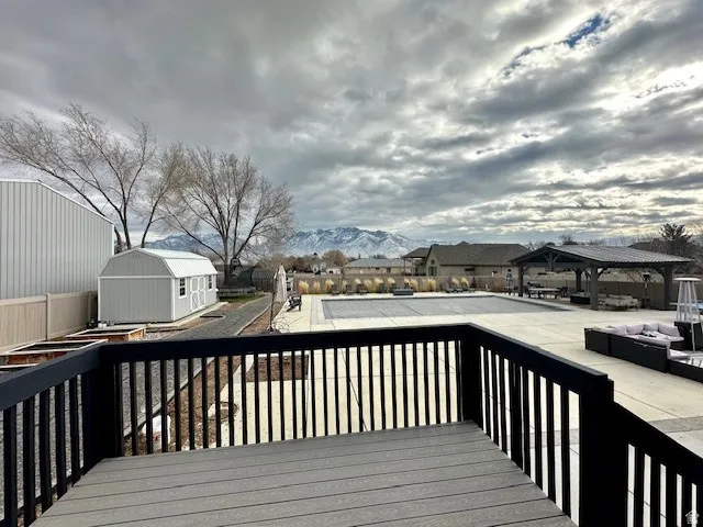 Deck with dark railing overlooking a paved patio with a covered pool and mountain backdrop