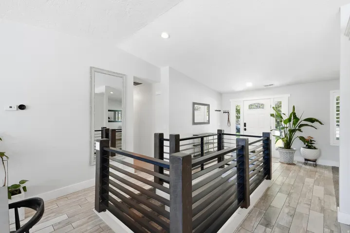 Modern hallway featuring horizontal slat railing with black metal framework, light wood-finish flooring, recessed ceiling lighting, and abundant natural light from multiple windows