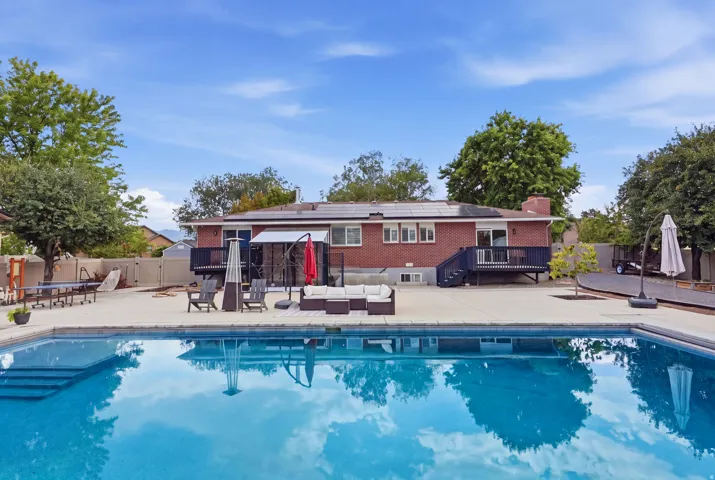 Resort-style swimming pool with crystal-clear water and surrounding concrete decking, anchored by a brick utility building with covered patio area and mature landscaping throughout the grounds