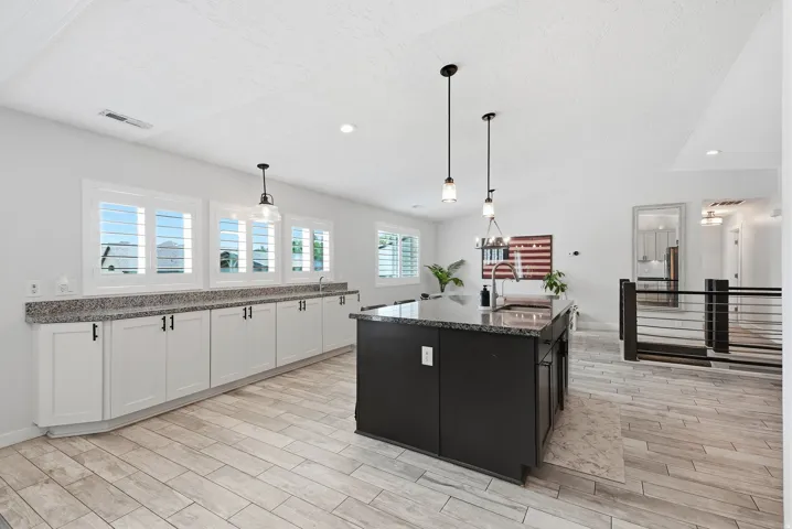 Modern kitchen featuring white shaker cabinetry, granite countertops, a dark-toned island, and pendant lighting